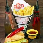 Best food photography of La Cresta sandwich meal, with french fries in a branded cone, a red chili pepper on top of the sandwich, and sauce bottles on the side.